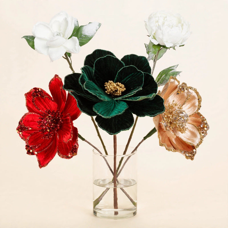 Floral stems arrangement with emerald peony, red and champagne magnolia, white magnolia and frosted peony in a glass vase on warm cream