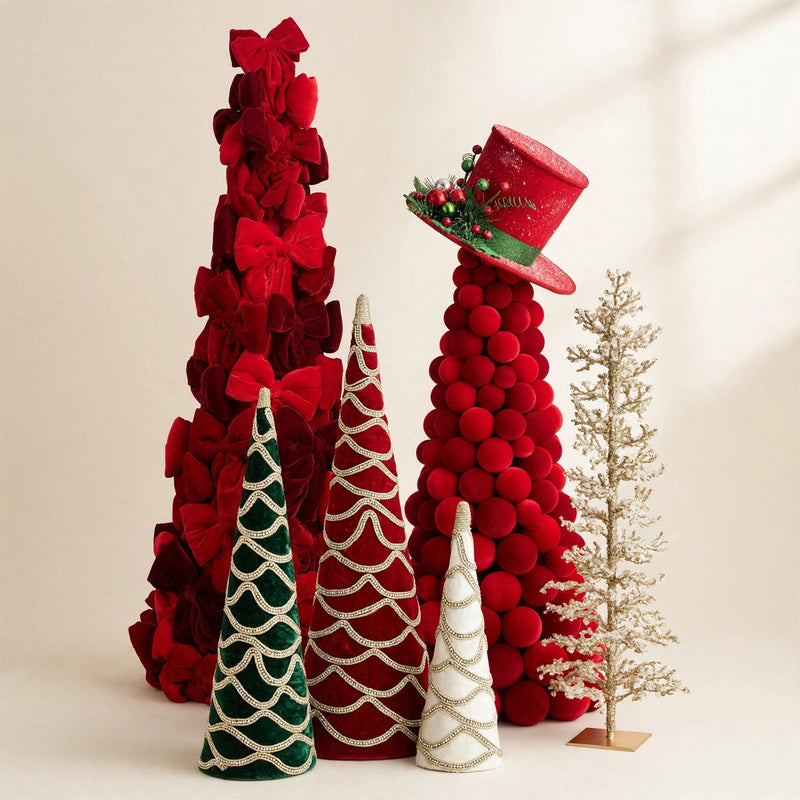 Red velvet bow topiary cone beside a red velvet ball topiary cone wearing a tilted red glitter top hat, green red and ivory velvet cone trio with gold swirl trim in front, slim champagne-gold icy pencil tree at the side, on a warm cream backdrop.