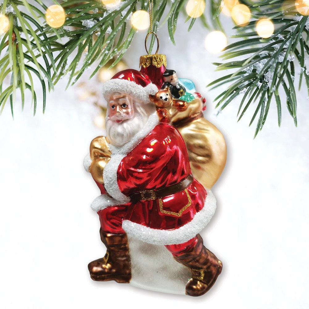 Red glass Santa ornament carrying a gold toy sack, styled against pine branches and warm lights.