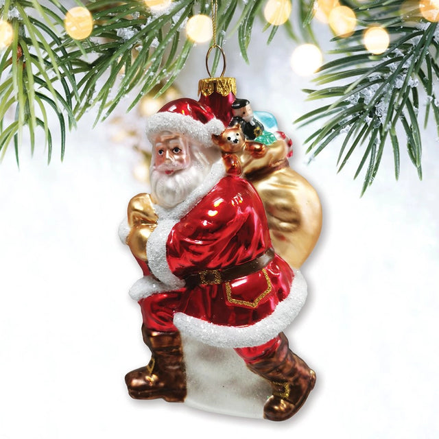 Red glass Santa ornament carrying a gold toy sack, styled against pine branches and warm lights.