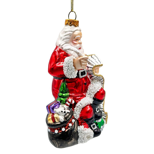 Red glass Santa ornament with his Christmas list and a black sack of gifts at his feet.
