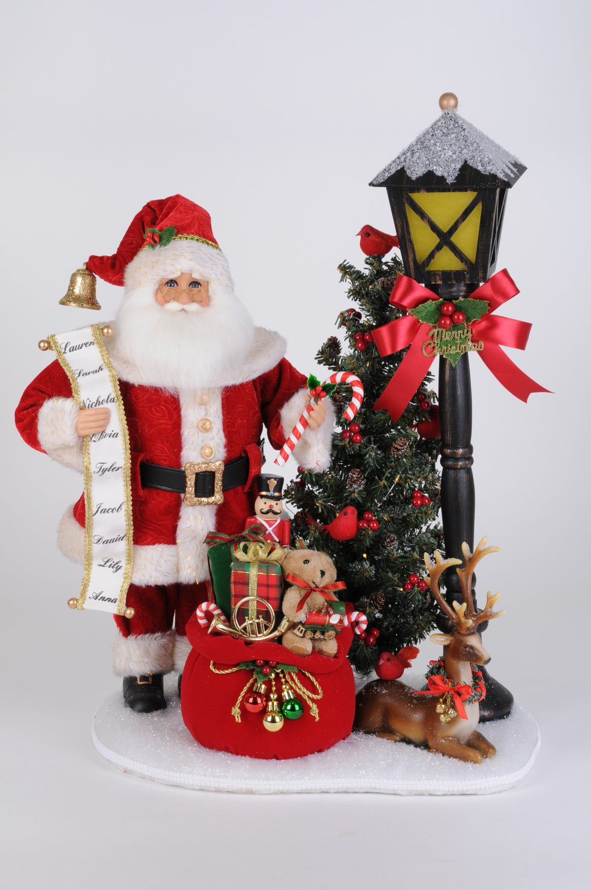 Santa figurine in a red suit beside a lighted lamp post and Christmas tree.